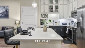 A modern kitchen with white cabinets, a central island, and stainless steel appliances. - Reluxme| Luxury 1BR in Uptown w/ Resort Amenities (Charlotte)