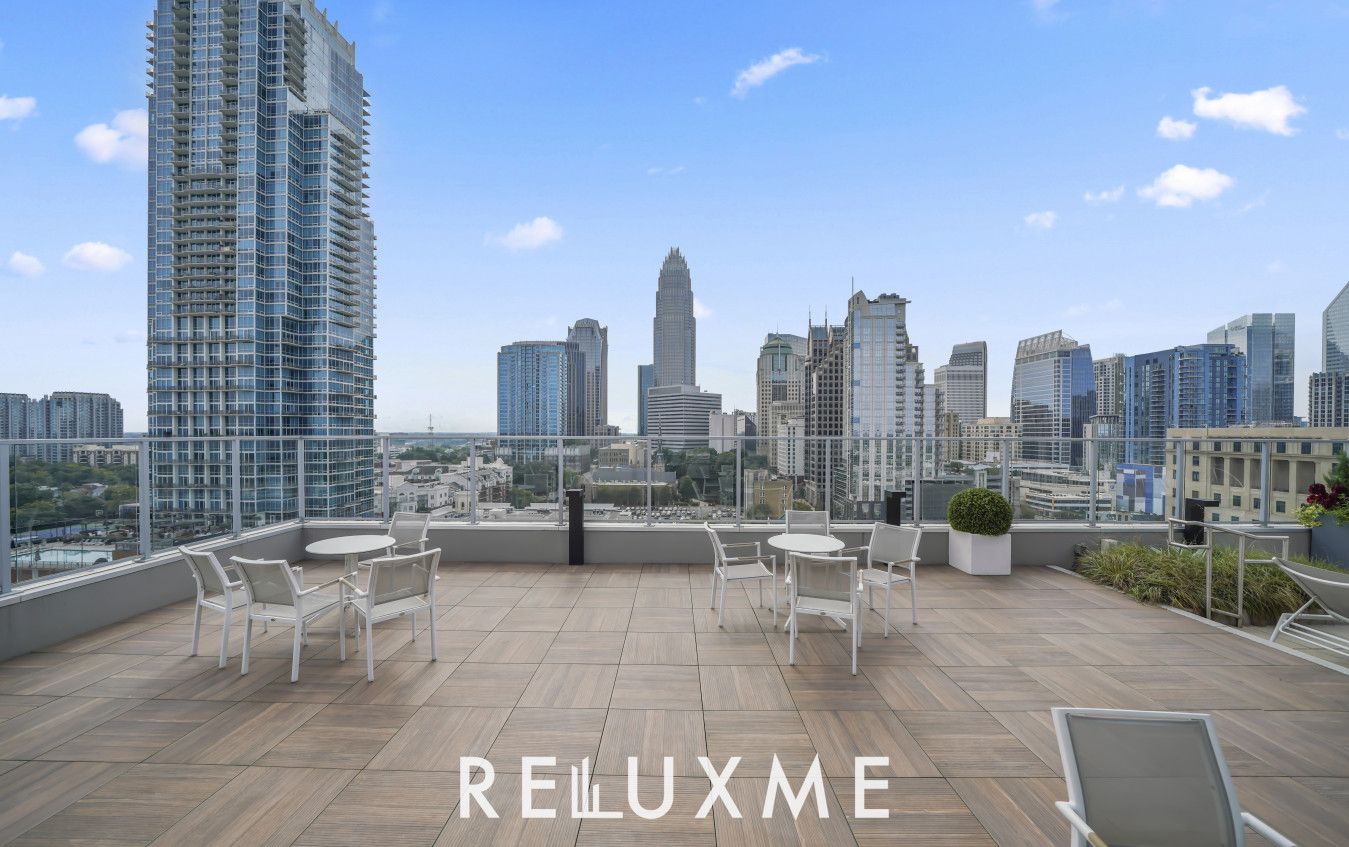A rooftop terrace with a city view, furnished with white chairs and tables, and the text "RELLUXME SHORT & LONG TERM STAYS".