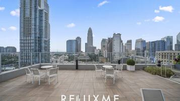 A rooftop terrace with a city view, furnished with white chairs and tables, and the text "RELLUXME SHORT & LONG TERM STAYS".