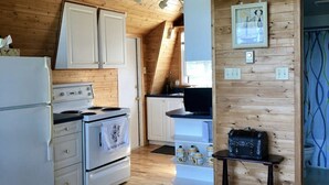 A wooden cabin kitchen with a refrigerator, stove, cabinets, and a small table. - Cabin on the beach. (Miramichi)