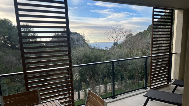 A balcony with a wooden table and chairs, a view of trees and a distant landscape. - Prestige view 411 by Avecoeur (Èze)