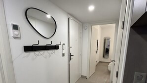 A hallway with a black doormat, a wall-mounted mirror, a smoke detector, and a door leading to a bathroom. - Prestige view 411 by Avecoeur (Èze)
