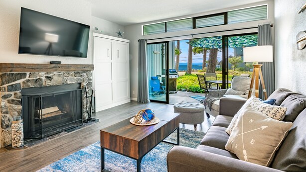 A living room with a stone fireplace, a flat-screen TV, a sofa, and a view of the outdoors.