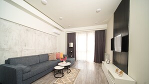 Un salon moderne avec un canapé gris, une petite table ronde et un téléviseur fixé au mur.