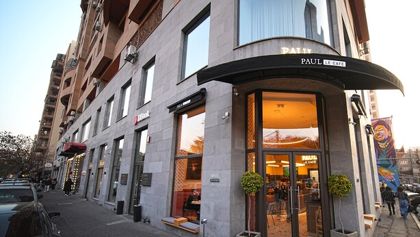 Un bâtiment avec une entrée incurvée, une enseigne indiquant « Paul Le Café » et une devanture visible avec un auvent rouge.