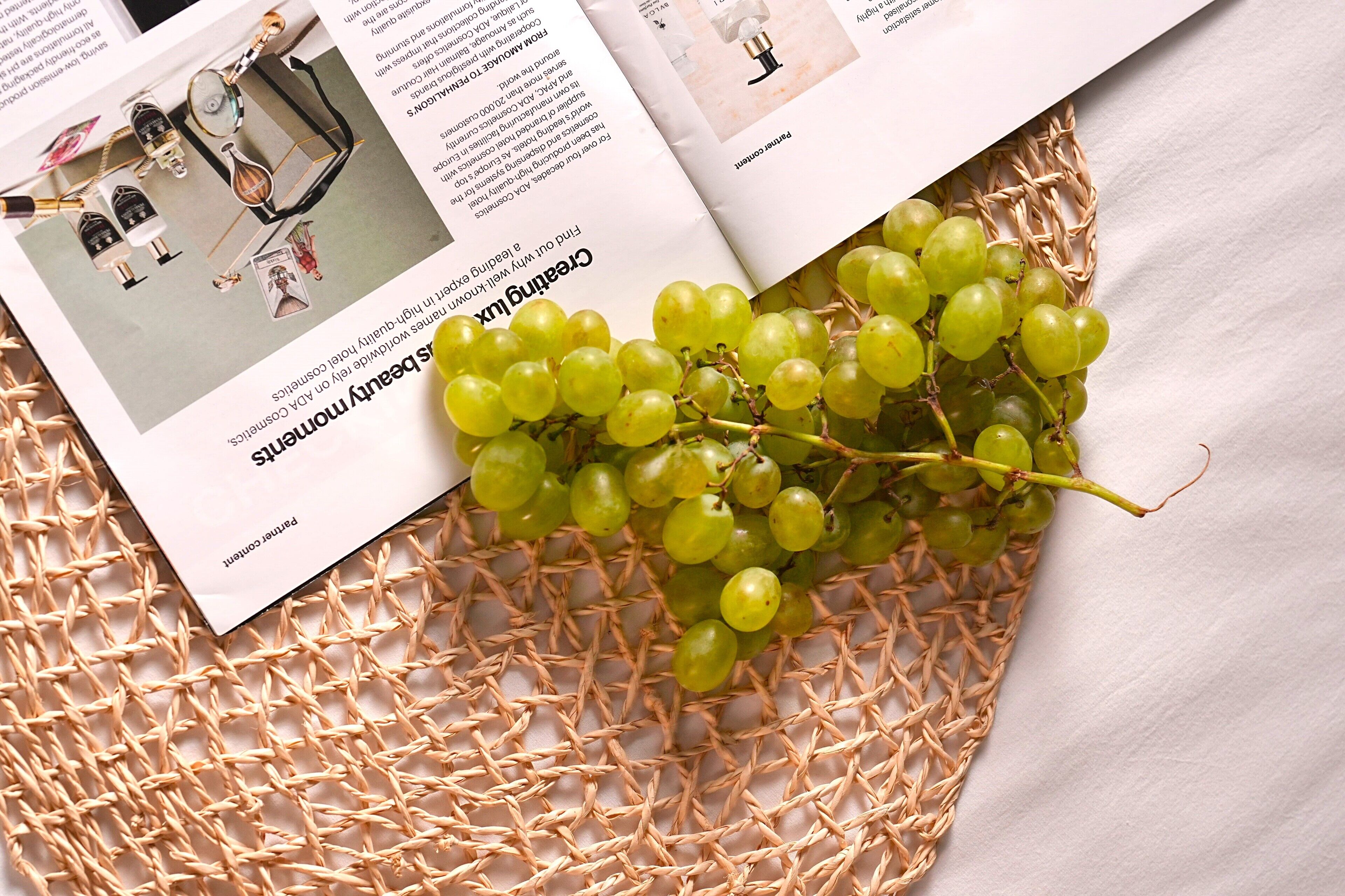 A magazine with a photo of a room layout, a wicker basket with green grapes, and text.