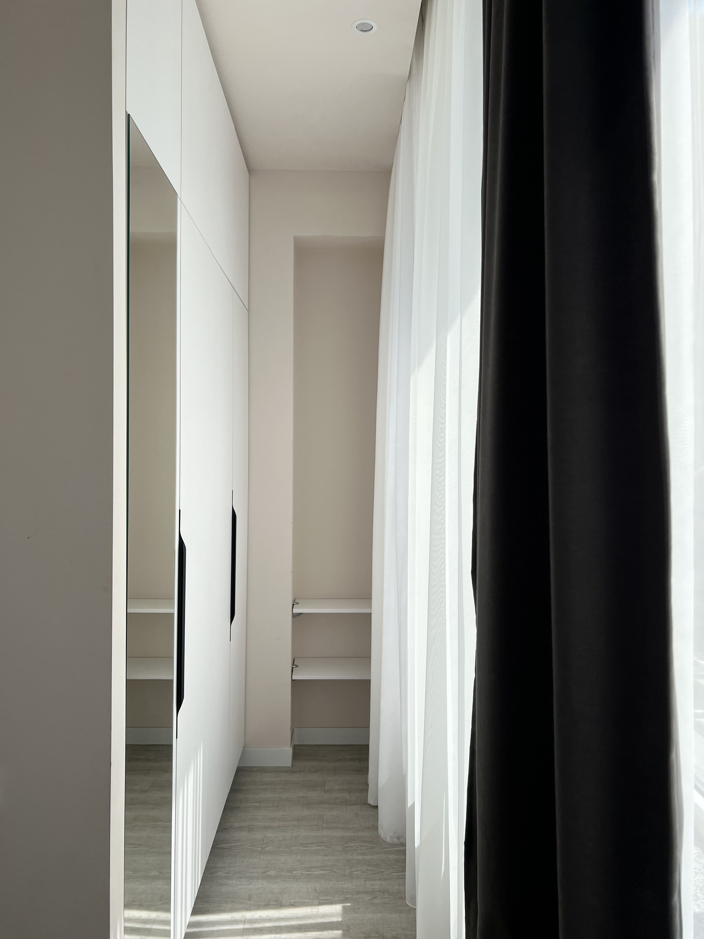A narrow hallway with white walls, a wooden floor, and a black curtain on the right.