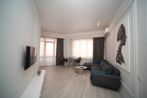Una sala de estar moderna con un sofá, un televisor, una mesa de centro y una zona de comedor con sillas.