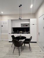 Een moderne keuken met witte kasten, een zwarte eettafel met vier stoelen en een magnetron op het aanrecht.