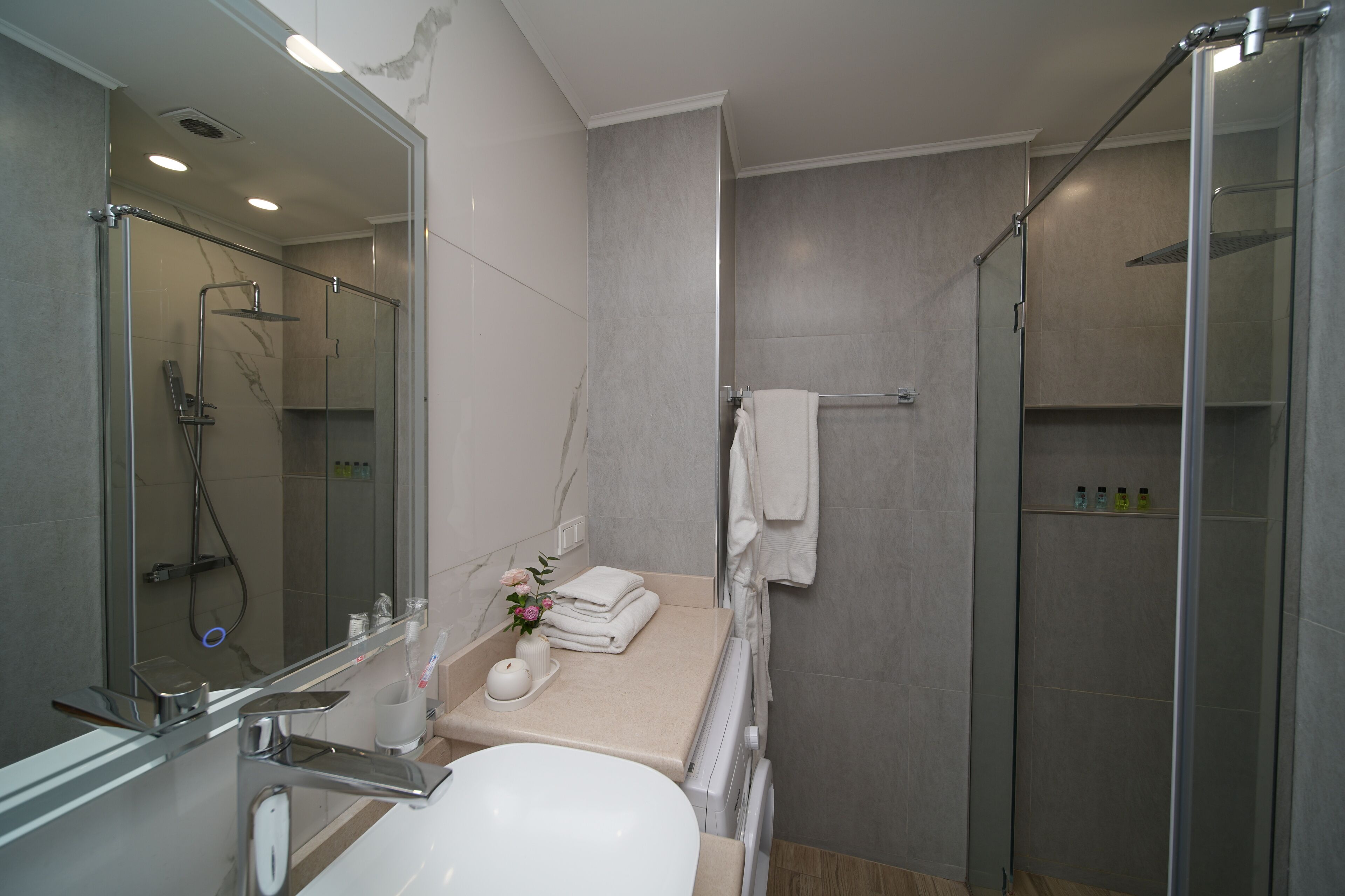 Un baño moderno con ducha de vidrio, un lavabo con espejo y un perchero para toallas.