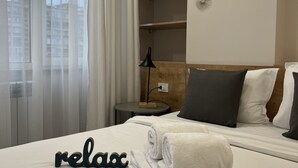 Un lit bien fait, avec des serviettes pliées et un panneau indiquant «détente», une table de chevet avec une lampe, et un mur orné de motifs décoratifs en forme de soleil.