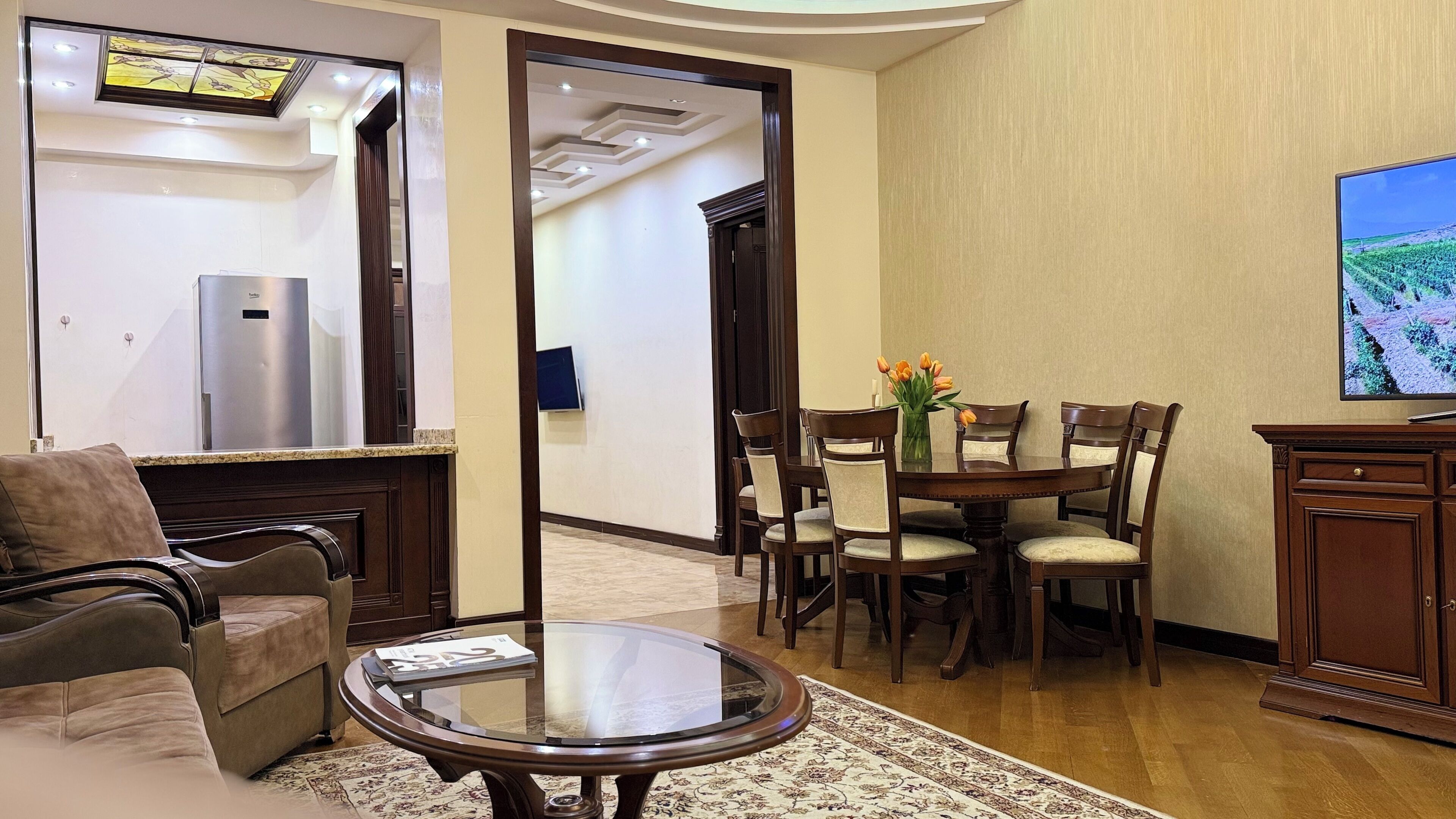 Un salon comprenant un canapé, une table basse avec un plateau en verre, une table à manger avec des chaises, un téléviseur et un réfrigérateur.