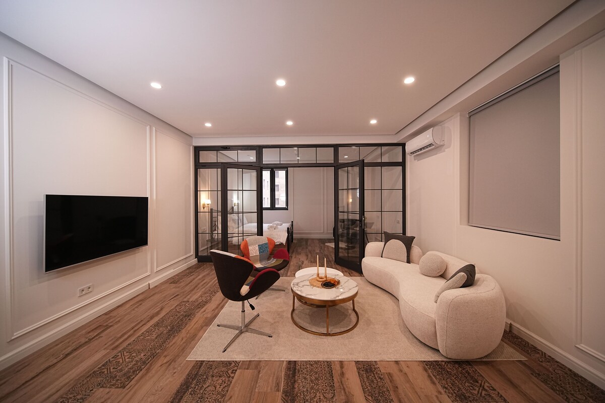 A modern living room with a flat-screen TV, a sofa, a coffee table, and a chair.