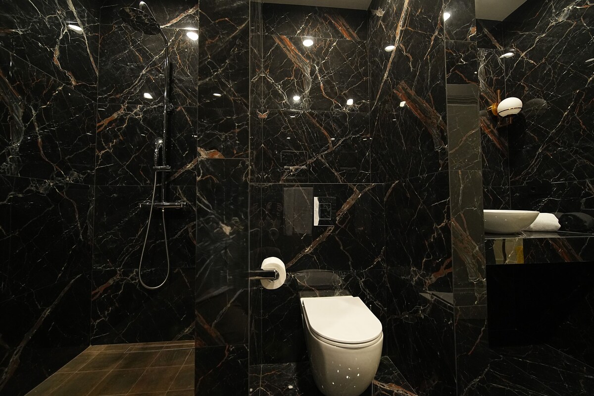 A modern bathroom with a marble wall, a toilet, and a shower area.