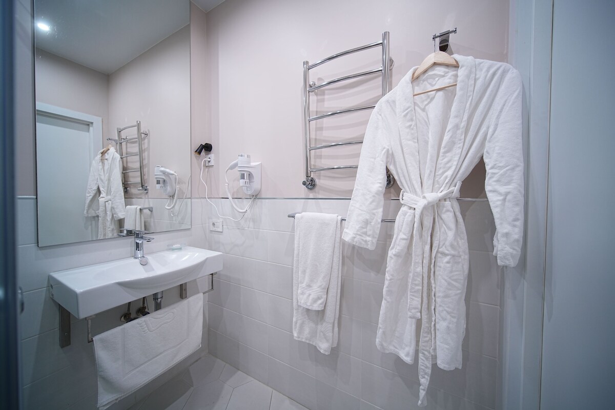 A modern bathroom with a white sink, mirror, towel rack, and a robe hanging on the wall.