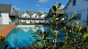 A swimming pool with a wooden deck, surrounded by a white building with a balcony. - Holiday Home in Pobierowo near Beach (Rewal)