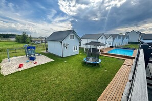 A residential backyard with a swimming pool, a trampoline, and a play structure.