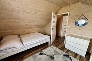 A small wooden room with a bed, a dresser, and a door leading to another room.