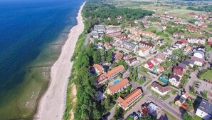 An aerial view of a coastal residential area with houses, a beach, and a lighthouse in the distance. - Holiday Home in Pobierowo near Beach (Rewal)