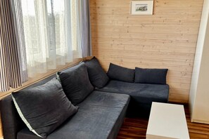 A corner sofa with cushions, a small white table, and a wooden wall with a picture frame.
