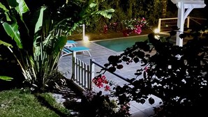 Uma área de piscina com pérgola, rodeada por vegetação exuberante e plantas floridas.