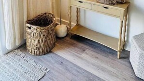 A room with a light-colored console table, a floor lamp, a woven basket, and a small decorative item on the wall. - 1BR Cottage Close to Beach! (Wildwood)