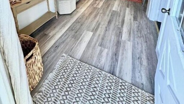 A room with a wooden floor, a red and white patterned rug, a sofa, a small table with a lamp, and wall decorations including a 'Beach Seashells Sand' sign. - 1BR Cottage Close to Beach! (Wildwood)