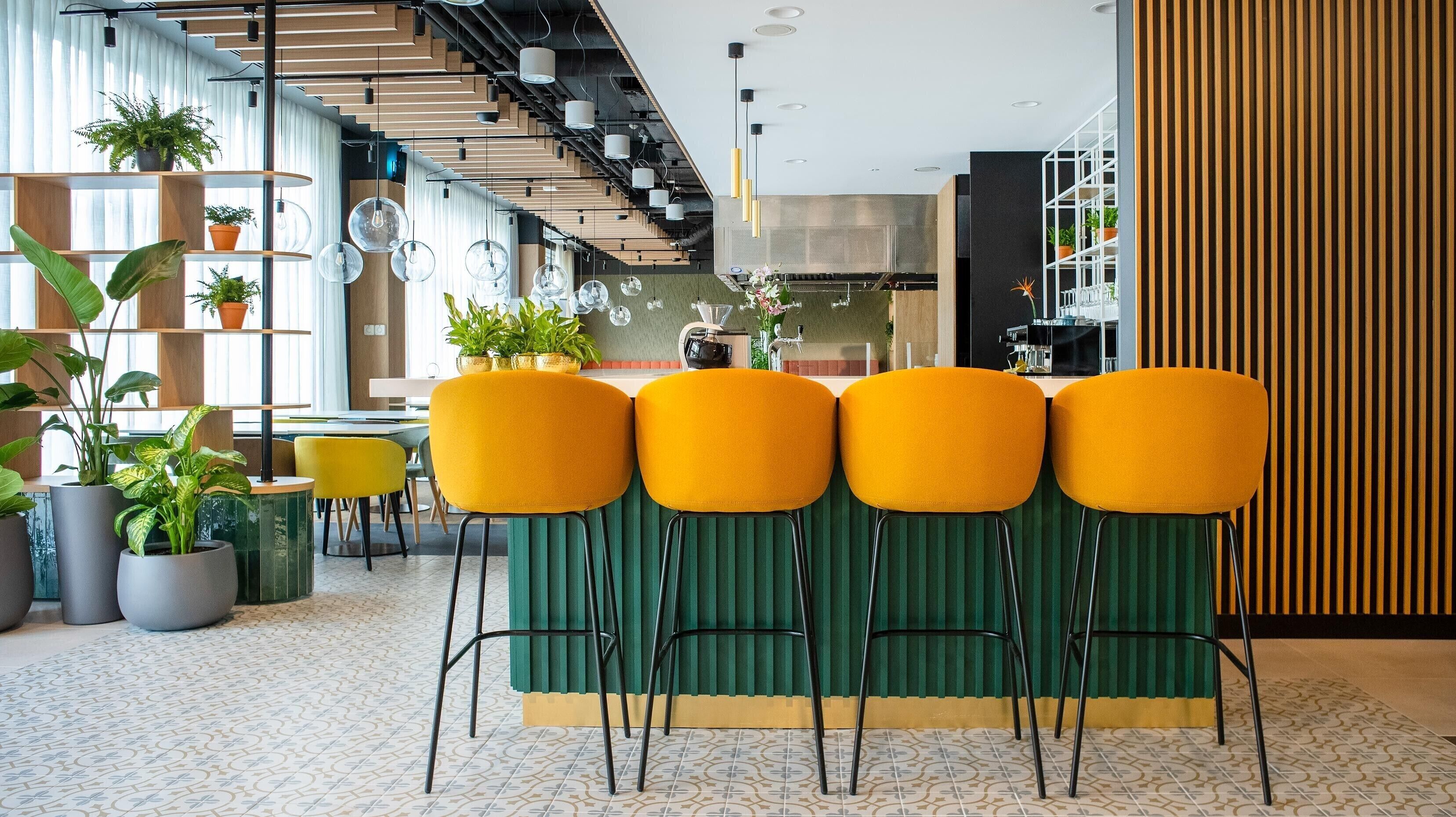 A modern interior with a green bar area, yellow chairs, and potted plants.