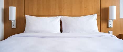Una cama con sábanas blancas, cabecera de madera y dos lámparas fijadas a la pared.