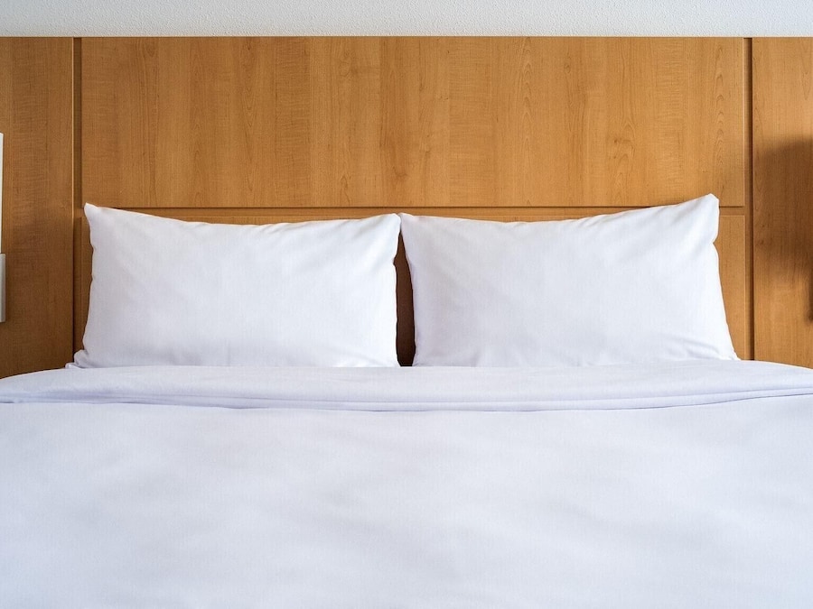 A bed with white linens, a wooden headboard, and two wall-mounted light fixtures.