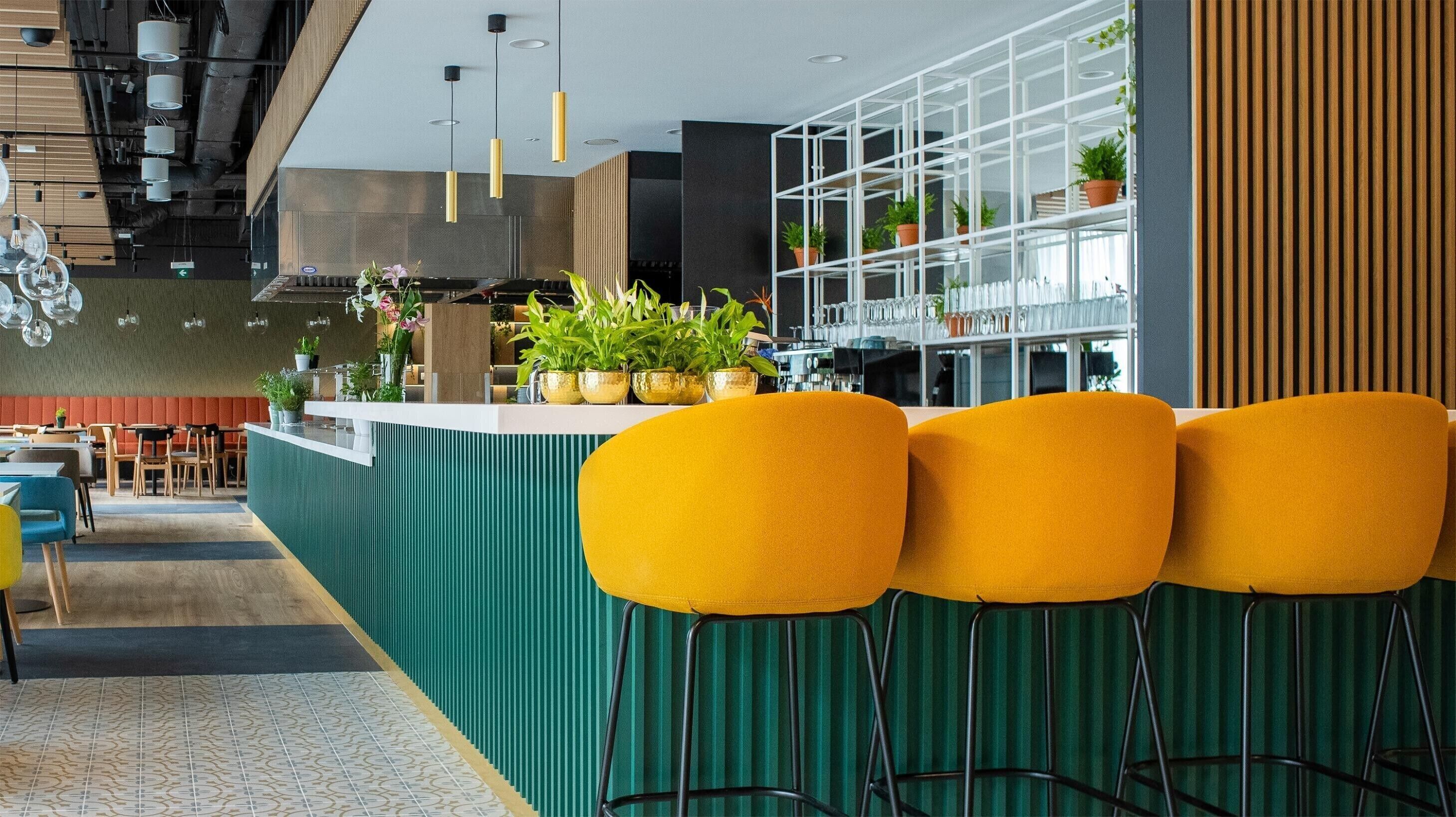 Un espace bar moderne avec un comptoir vert, des tabourets jaunes et des plantes en pot.