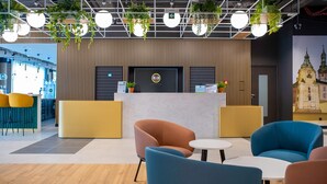 Un área de recepción de hotel con diseño moderno, que incluye un mostrador de recepción, zona de asientos con sillas y un mural grande en la pared.