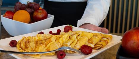 Ein Teller mit Pfannkuchen und Früchten, im Hintergrund eine Fruchtschale.