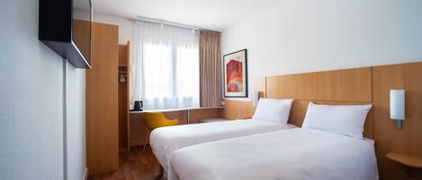 Habitación de hotel con dos camas, un escritorio, una silla, una ventana con cortinas y una lámpara de pared.
