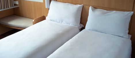 Une chambre d’hôtel avec deux lits simples, une table de chevet et une lampe fixée au mur.