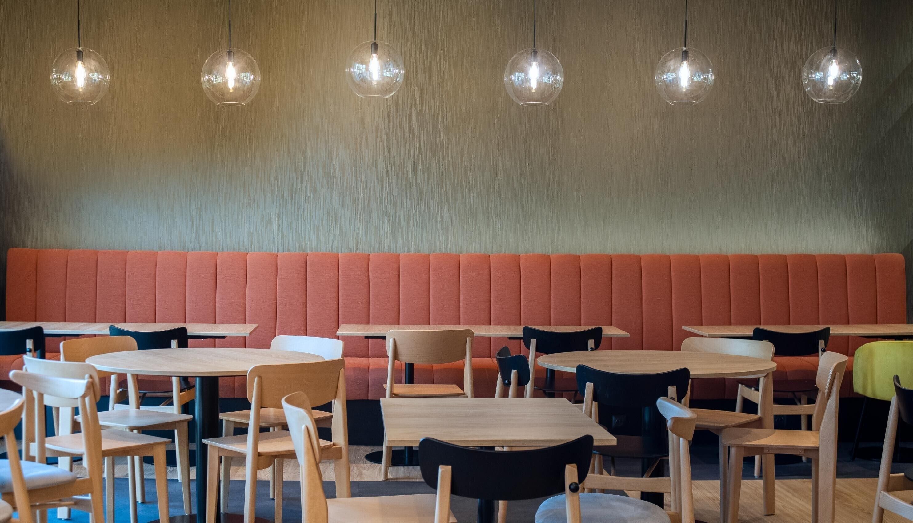 A restaurant interior with round tables, chairs, and a red cushioned bench.