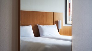 A hotel room with a wooden headboard, two white pillows, and a bedside lamp. - B&B HOTEL Kielce Centrum (Kielce)