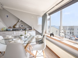 Una cocina moderna con una mesa de vidrio, sillas blancas y vistas al mar a través de amplios ventanales.