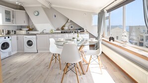A modern kitchen with a dining area, large windows, and a view of the sea. - The Penthouse @ No 5 (Lyme Regis)