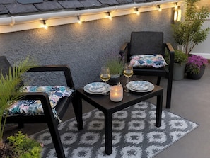 An outdoor seating area with two chairs, a table, and string lights. - Tŷ Capel Bach (Bangor)