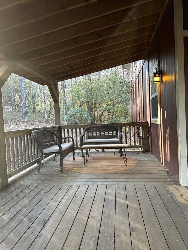 Relax on the deck with a bench and wicker chair, surrounded by trees and a wooded landscape.