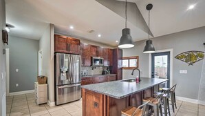 Una cocina moderna con armarios de madera, electrodomésticos de acero inoxidable, una isla central con taburetes altos y una lámpara colgante.