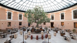 A spacious indoor area with a central bar, multiple seating arrangements, and a large tree in the middle.