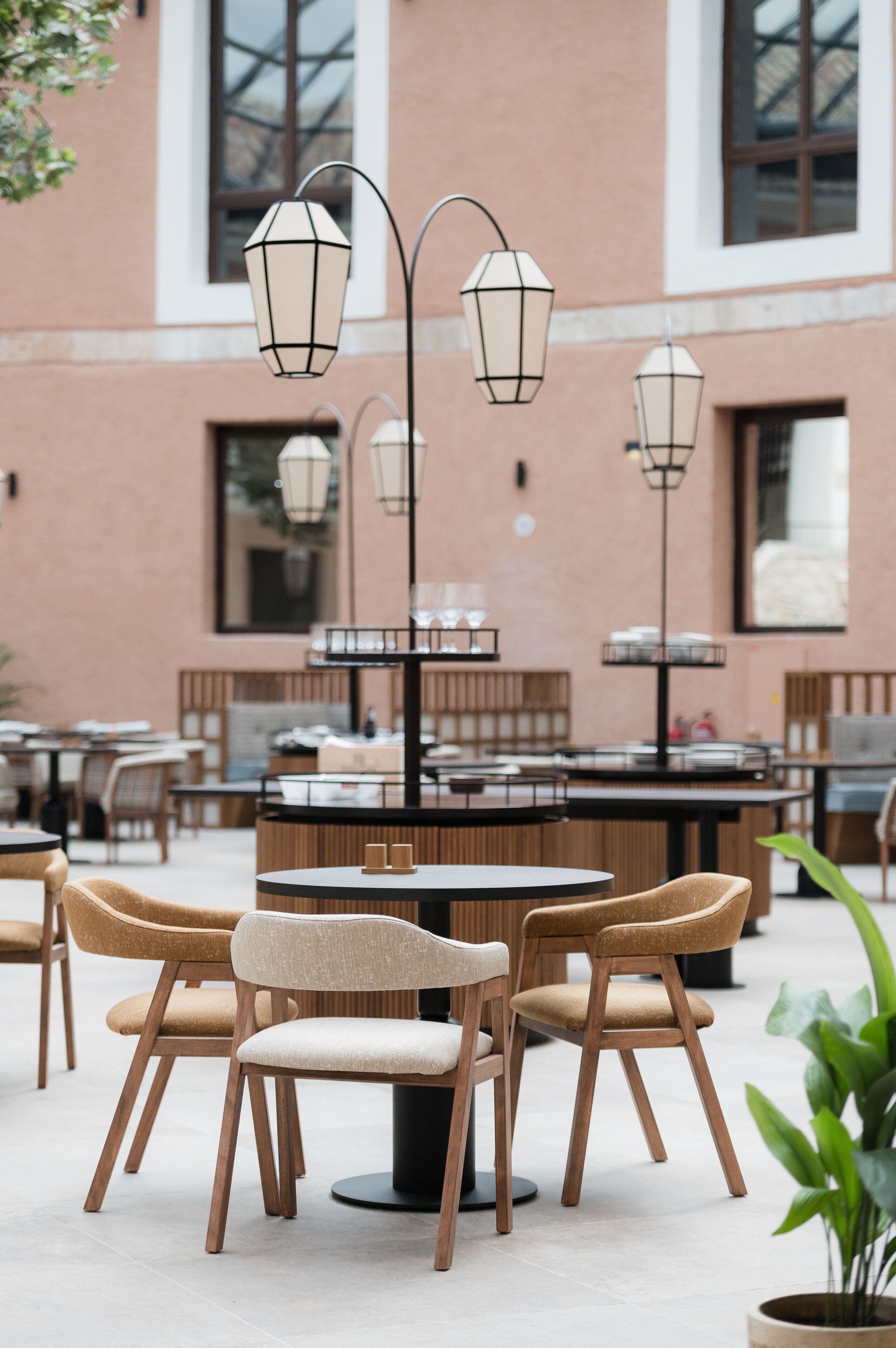 Een buitenruimte met ronde tafels en stoelen, omringd door een gebouw met grote ramen en bakstenen.