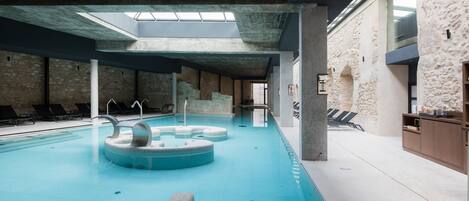 An indoor swimming pool with a skylight, stone walls, and lounge chairs.