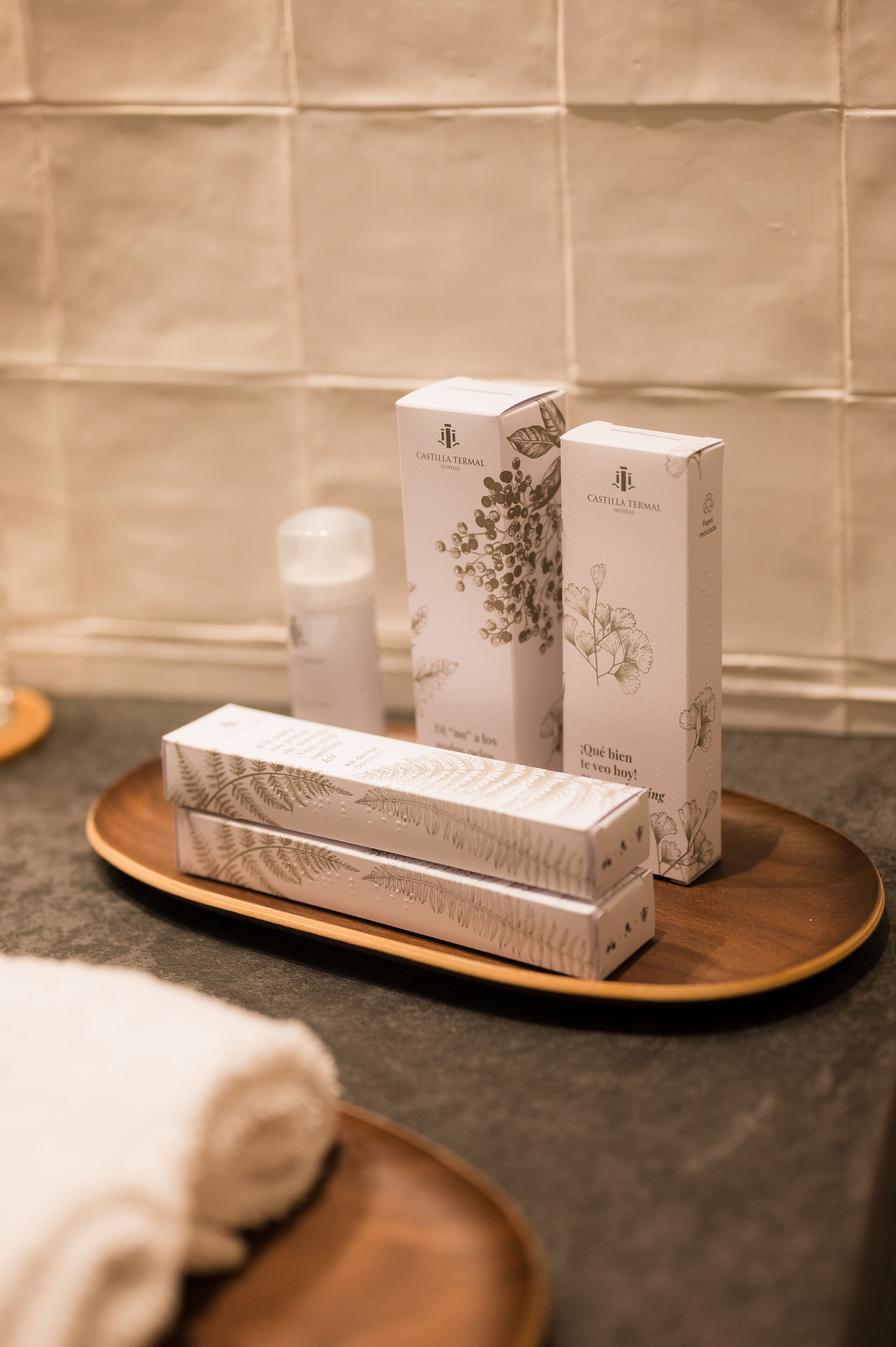 A bathroom with a wooden tray holding three boxes of Castilla Termal products, a white towel, and a bottle.