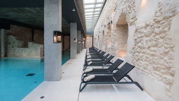 An indoor swimming pool with lounge chairs and a stone wall.
