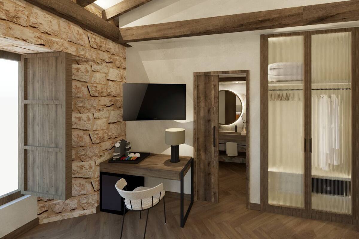 Een kamer met een stenen muur, houten balken, een bureau met stoel, een televisie en een schuifdeur naar een badkamer met spiegel en handdoekhouder.
