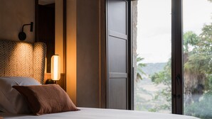 Une chambre à coucher avec un lit, une table de chevet avec une lampe et une grande fenêtre donnant sur un paysage verdoyant.
