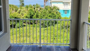 Une terrasse couverte offrant une vue sur un quartier résidentiel, avec notamment une maison dotée d’un toit turquoise et un palmier.
